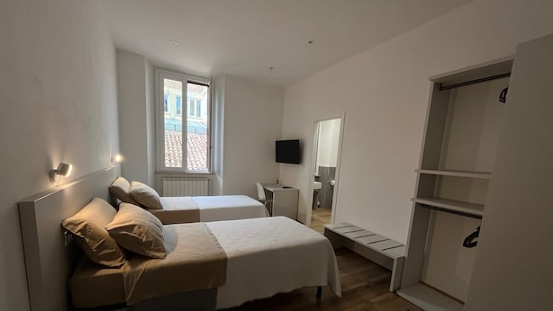 Een slaapkamer met twee bedden, een bureau, een televisie en een kledingkast.