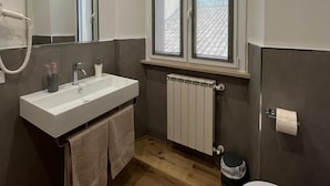 Een badkamer met een wit wastafelmeubel, spiegel en raam.