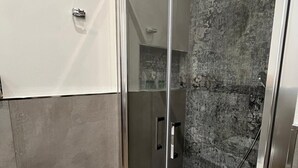 Een moderne badkamer met een douchecabine van glas, een houten vloer en een gestructureerde wand.