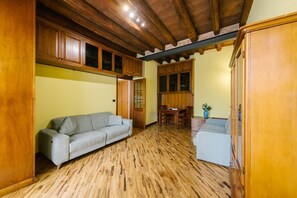 Ein Zimmer mit Holzboden, einem grauen Sofa, einem Esstisch mit Stühlen und Holzausbau.