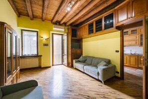 Ein geräumiger Raum mit Holzboden, einer Couch, einem Fernseher und Holzschränken.