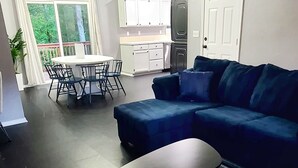 A living room with a dark blue sectional sofa, a round coffee table, and a dining area with a table and chairs. - Bella Vista Base Camp: Biking, Trails & Adventure (Bella Vista)