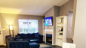 A modern living room with a round white table, blue chairs, a dark floor, a sofa, a TV, and a fireplace. - Bella Vista Base Camp: Biking, Trails & Adventure (Bella Vista)