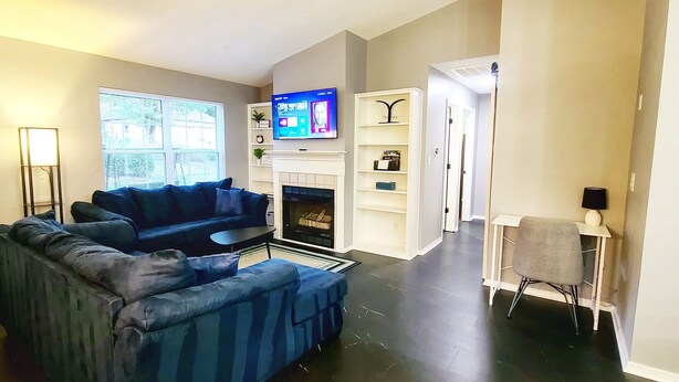 A living room with a sectional sofa, a flat-screen TV, a fireplace, and a bookshelf. - Bella Vista Base Camp: Biking, Trails & Adventure (Bella Vista)