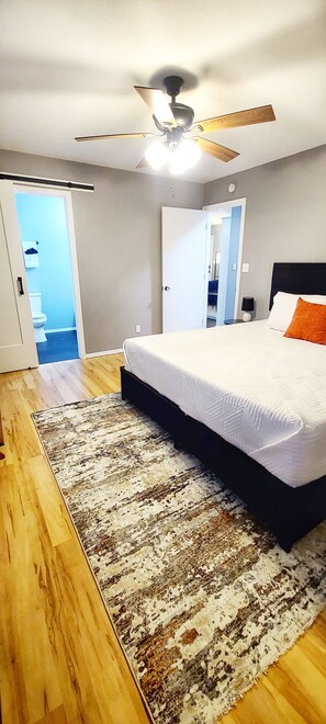 Une chambre avec un lit, un ventilateur de plafond, un plancher en bois et une vue sur l’extérieur.