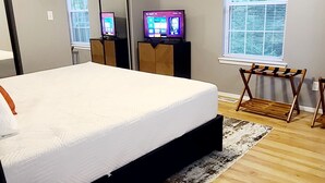 A bedroom with a bed, a ceiling fan, a TV, a window with blinds, and a wooden floor. - Bella Vista Base Camp: Biking, Trails & Adventure (Bella Vista)