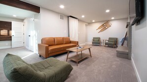 A living room with a brown sofa, a green armchair, a wooden coffee table, and a television mounted on the wall.