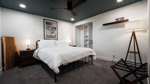 A bedroom with a bed, nightstand, lamp, ceiling fan, and a wooden ladder.