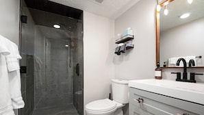 A modern bathroom with a glass-enclosed shower, a white toilet, a white sink with a black faucet, and a mirror above the sink.