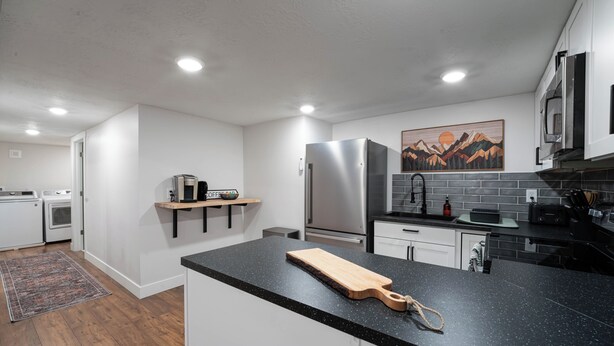 A modern kitchen with white cabinets, a black countertop, stainless steel appliances, and a wooden cutting board.