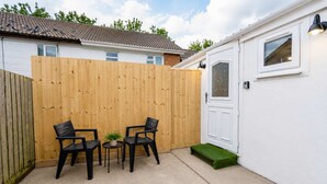Ein Patio mit Holzlattenzaun, zwei schwarzen Stühlen, einem kleinen Tisch und einem Blumentopf.