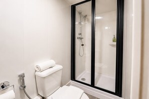 Moderni kylpyhuone, jossa on wc, lasiseinällä varustettu suihku ja valkoinen pesuallas.