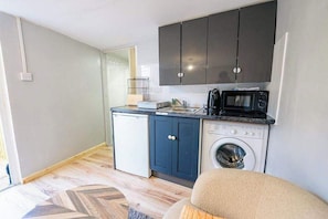 A compact kitchen with a washing machine, a microwave, and a small refrigerator.