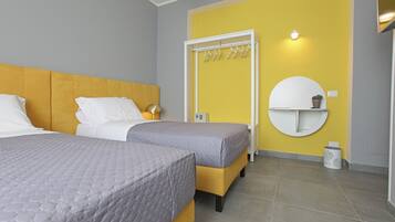 Quarto de hotel com duas camas, parede amarela de destaque, espelho redondo e porta-toalhas fixado na parede.