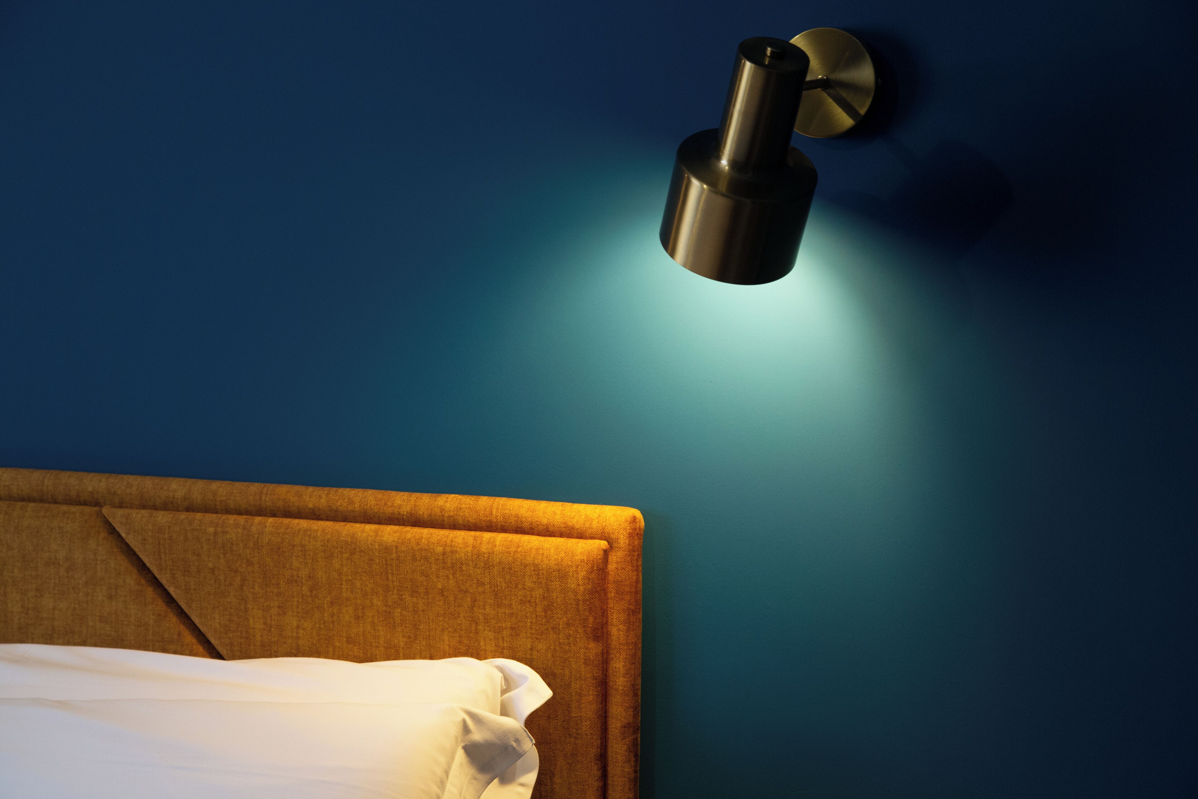 A bed with a headboard, a wall-mounted light fixture, and a textured wall.