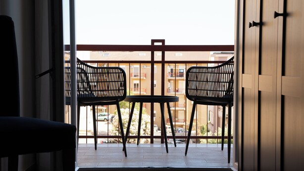 A balcony with two chairs and a table, a view of buildings, and a door to the right. - Malù Bed & Breakfast (Agrigento)