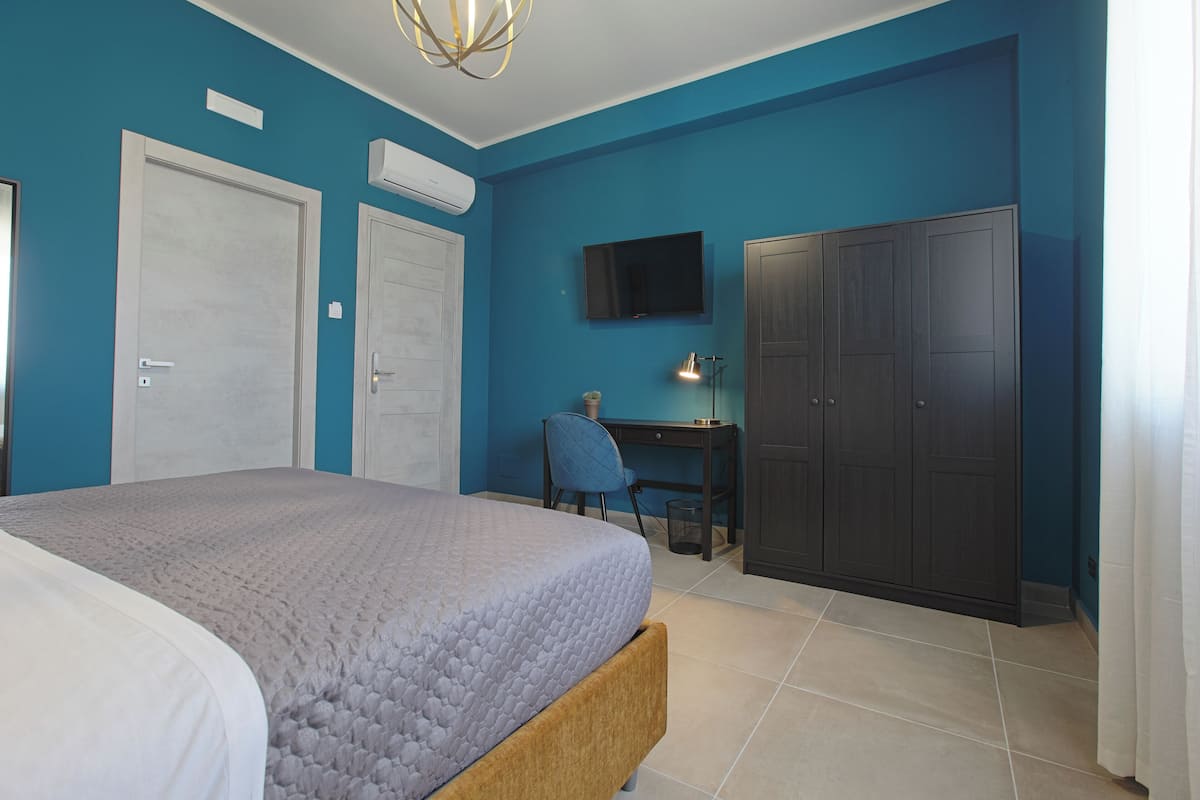 A bedroom with a bed, a desk, a chair, a wardrobe, and a television.