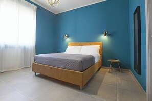 A bedroom with a bed, a small table, and a wall-mounted light fixture. - Malù Bed & Breakfast (Agrigento)