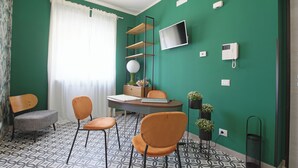 A room with a green wall, a desk with a chair, a TV, a telephone, and a window with curtains. - Malù Bed & Breakfast (Agrigento)