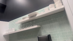 Cucina con scaffali bianchi, un tostapane e una parete di fondo piastrellata.