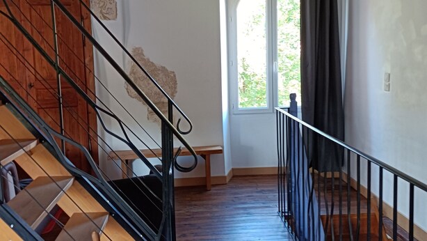 Eine Treppe mit Holzdielen und Metallgeländern, die zu einem Raum mit Steinwand und Fenster führt.