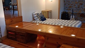 Ein gemütliches Schlafzimmer mit Schlafbox, einem kleinen Holzkabinett und einer Gitarre an einer Steinwand.