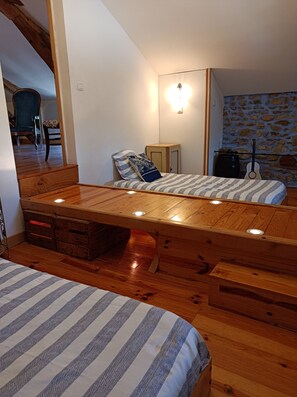 Une chambre avec un lit en mezzanine, un petit bureau, une guitare et un mur en pierre.