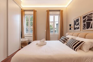 Habitación de hotel con una cama grande, dos ventanas con cortinas, un lavamanos y una obra de arte en la pared.