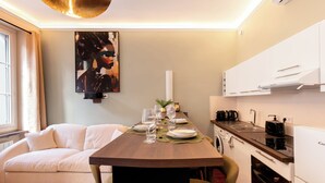 A modern kitchen with white cabinets, a dining table set with plates and glasses, and a sofa in the adjacent living area. - Cocon Heliot hypercentre Toulouse métro A&B Jean Jaurès - Pl. Wilson - Capitole (Toulouse)