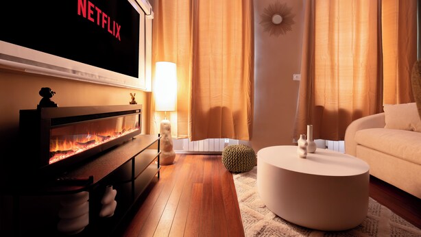 A living room with a fireplace, a flat-screen TV displaying 'NETFLIX,' a sofa, a round coffee table, and a lamp. - Cocon Heliot hypercentre Toulouse métro A&B Jean Jaurès - Pl. Wilson - Capitole (Toulouse)