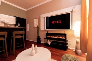 A living room with a TV displaying 'NETFLIX,' a fireplace, a kitchen area, and a seating arrangement. - Cocon Heliot hypercentre Toulouse métro A&B Jean Jaurès - Pl. Wilson - Capitole (Toulouse)