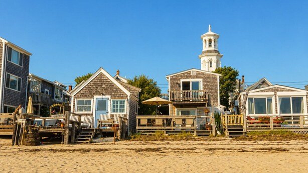Ein Küsteneigentum mit mehreren Häusern, einem Leuchtturm und einem Sandstrand.