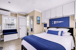 A bedroom with a large bed, a nightstand, a bedside table, a window with blinds, a door, and a mirror. - *NEW* Waterfront Studio - Bay Views, Steps to Comm St (Provincetown)