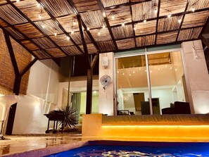 An indoor pool area with a thatched roof, a seating area, and a large window. - Villa & Pool Cascada - Tequesquitengo Lake View (Tequesquitengo)