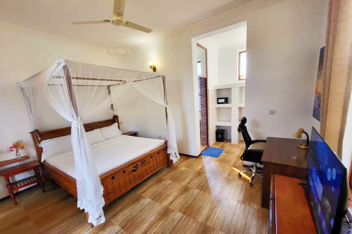 Un dormitorio con una cama con dosel, un escritorio con silla, una computadora y un ventilador de techo.