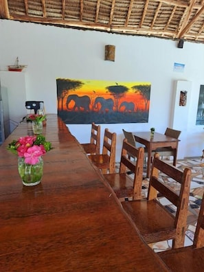 A long wooden table with chairs, a painting of elephants, and a thatched roof. - Mimi na Wewe Bungalows Hotel (Nungwi)