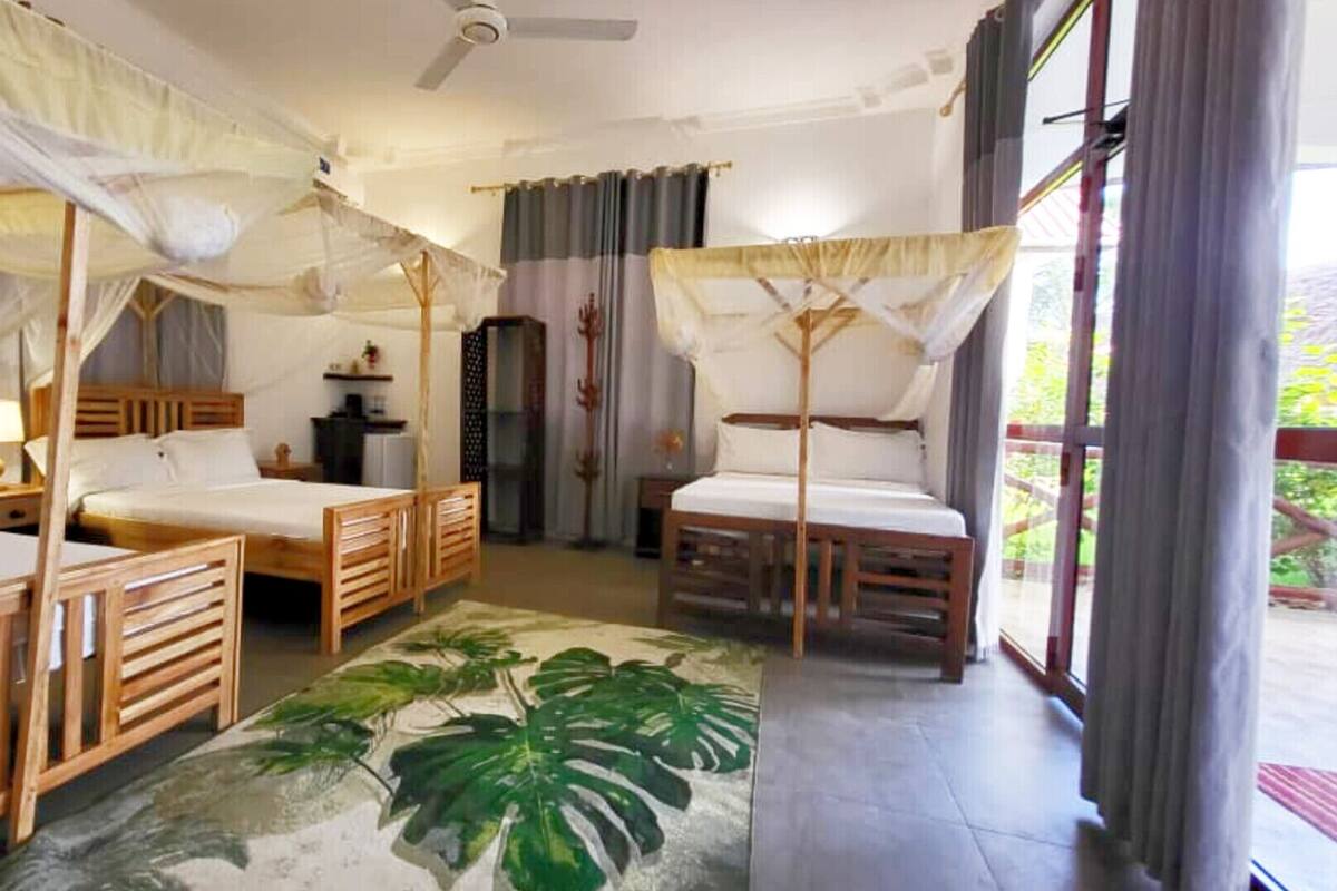 Habitación con dos camas, un ventilador de techo, una mesita pequeña, una planta y vistas al exterior.