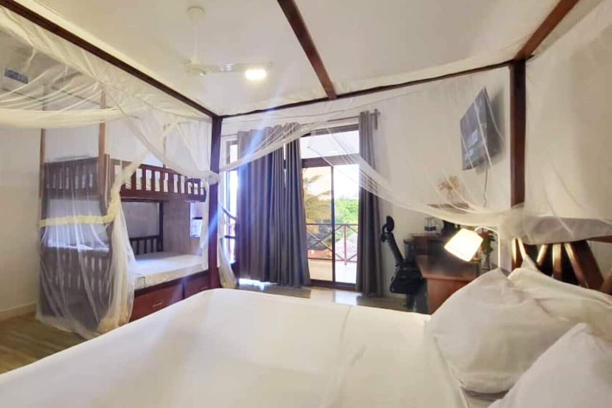Una habitación con cama, una mesita, una silla, un ventanal con cortinas y una puerta que da al exterior.