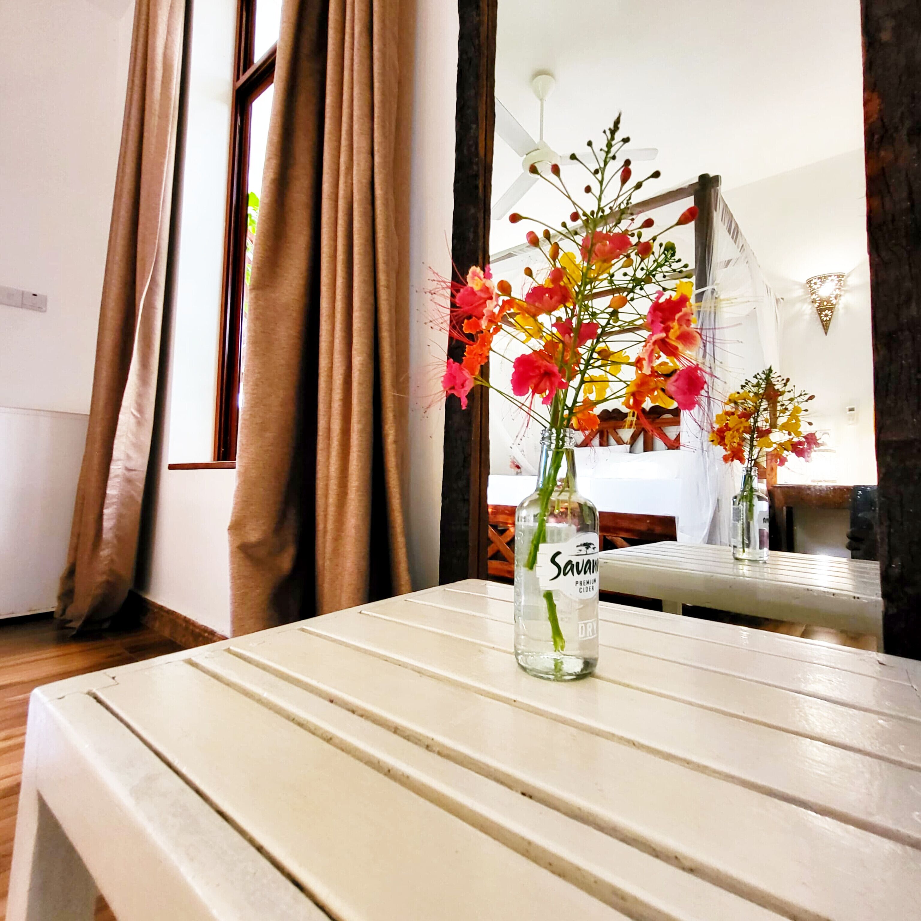 Une pièce avec une table, une bouteille de cidre Savana Premium et un miroir qui reflète une fenêtre avec des rideaux.