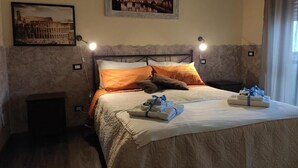 A bed with a white comforter, two orange pillows, and a blue towel with a gift. - Vatican Living Rome (Rome)