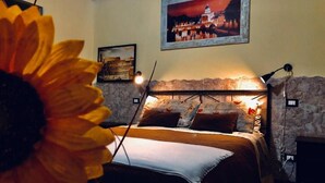 A bedroom with a stone wall, a bed with a white sheet, a framed picture above the bed, and a large sunflower in the foreground. - Vatican Living Rome (Rome)