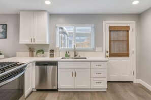 A modern kitchen with white cabinetry, a stainless steel dishwasher, and a window with blinds. - Two-Private Units/Sleep 9/Pool&Spa/Parking/AC (San Diego)