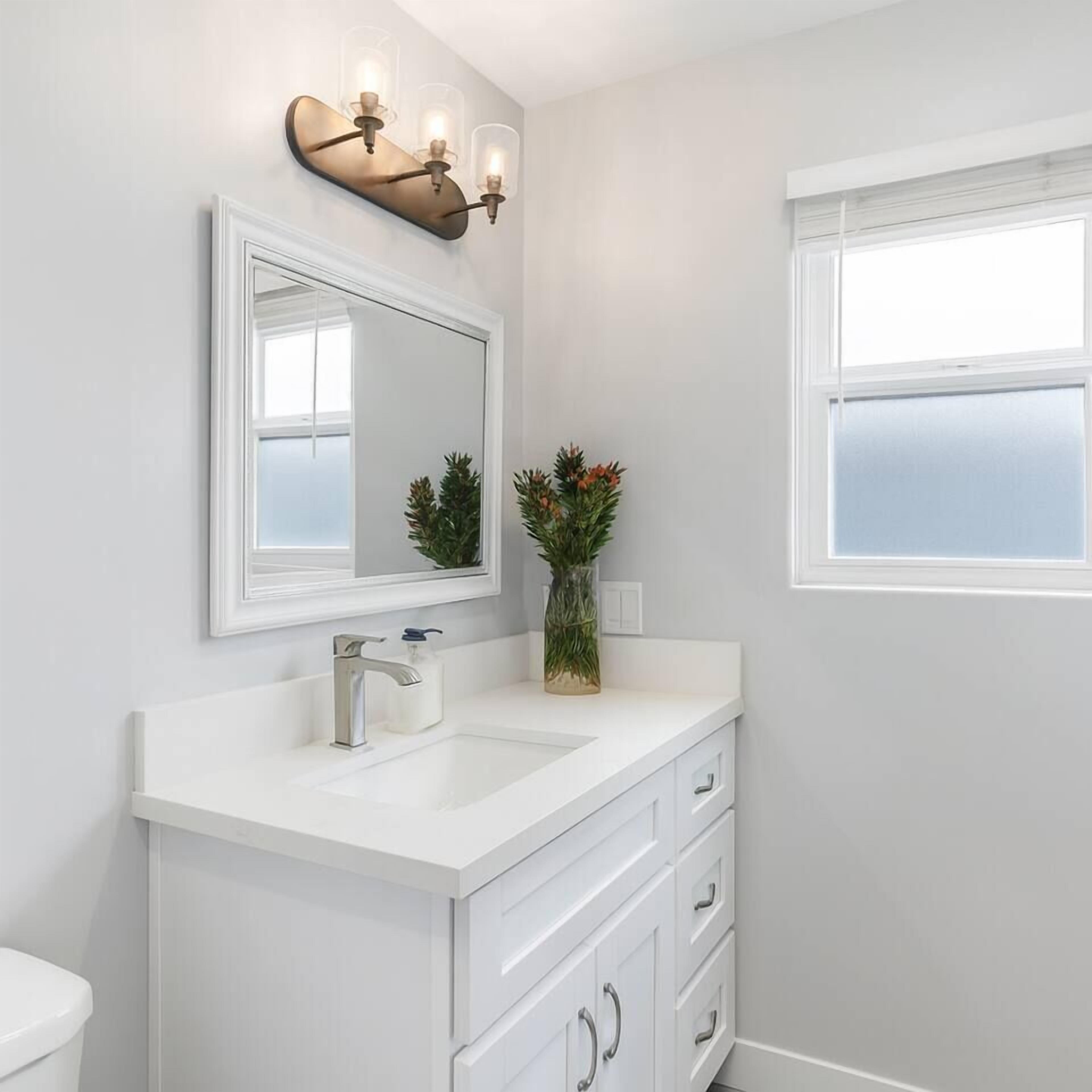 A bathroom with a white vanity, a large mirror, a wall-mounted light fixture, and a window.