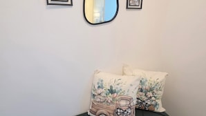 Un sofá verde con cojines estampados, un espejo y dos cuadros en la pared.