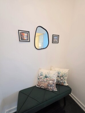 A green sofa with floral cushions, a mirror, and two framed pictures on the wall. - Executive condoCN Tower| Leafs| Raptors| Harbourfront| Balcony (Toronto)