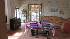 Une pièce avec un sol carrelé, une table entourée de chaises, un canapé, une bibliothèque et un téléviseur.