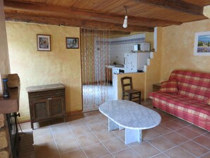 A living room with a sofa, a table, a kitchen in the background, and a wooden ceiling. - Country house.  Alpes de Haute-Provence (Clumanc)