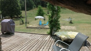 Une terrasse en bois avec un barbecue abrité, un parasol et un fauteuil de relaxation.