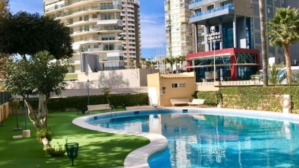 Una piscina de borde curvo, rodeada de follaje y junto a edificios altos.