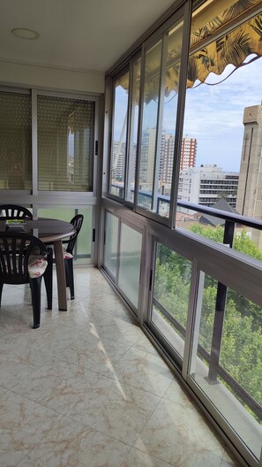 A balcony with a dining table and chairs, large windows, and a view of city buildings. - Benidorm, glazed terrace, 150m from Levante beach with parking and swimming pool (Benidorm)